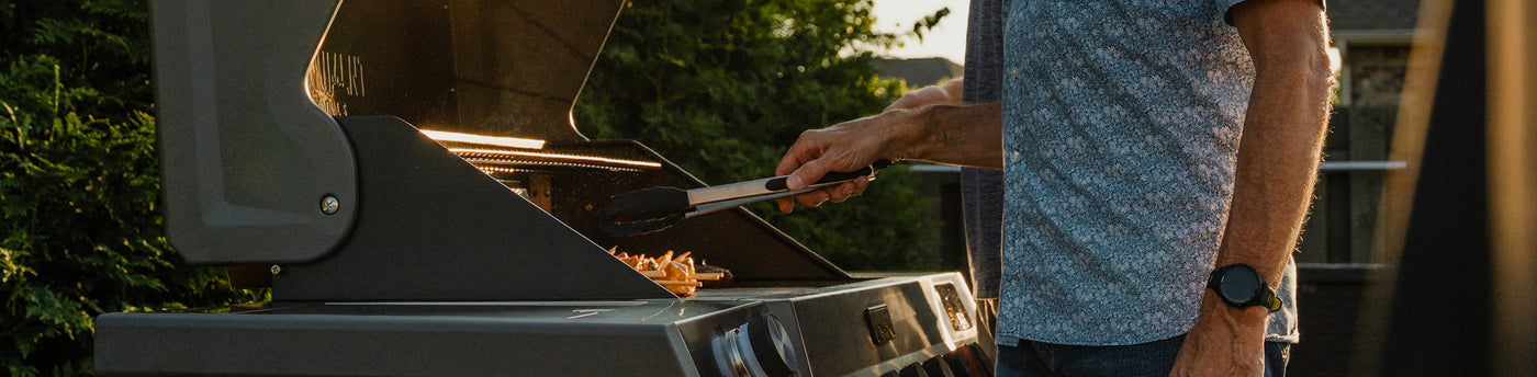 Person grilling outdoors with a focus on the grill and hands