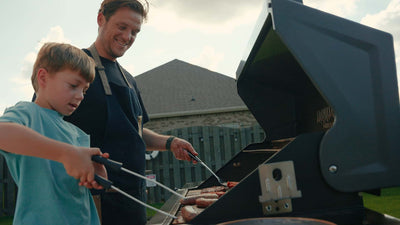 Man and child grilling hot dogs on a barbecue grill outdoors.