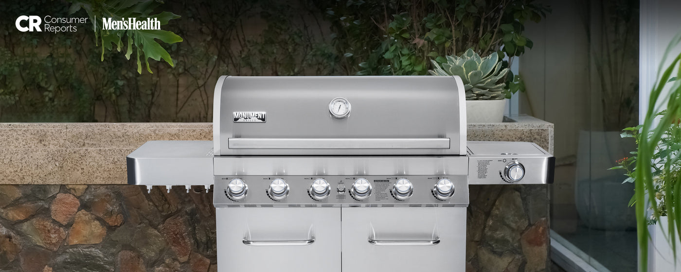 Stainless steel grill on a patio with plants and stone wall in the background