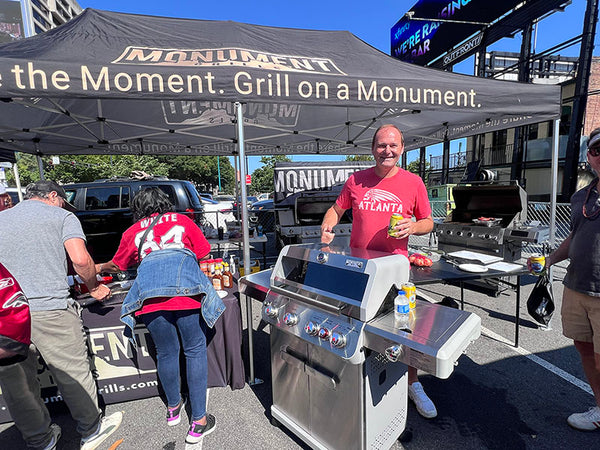 Man grilling at a Monument event with promotional tent and branding.