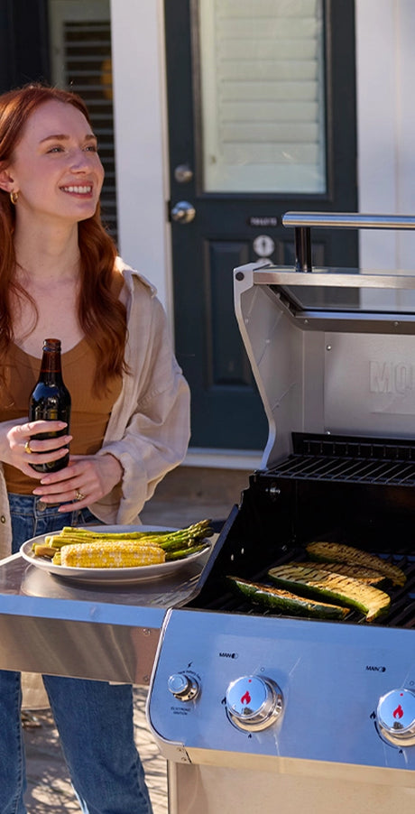 Woman grilling vegetables on a portable grill outside a house.
