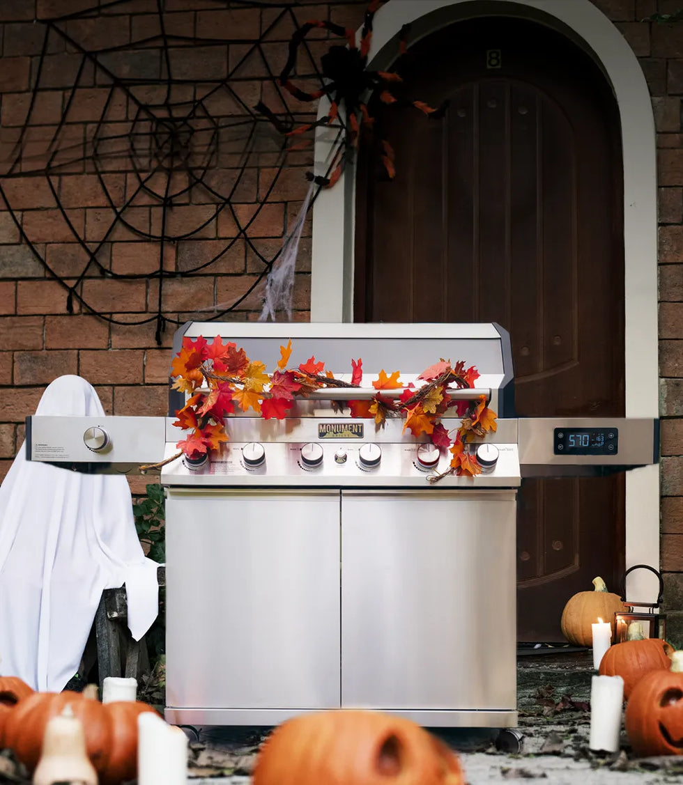 Outdoor grill with autumn leaves and pumpkins in front of a brick wall.