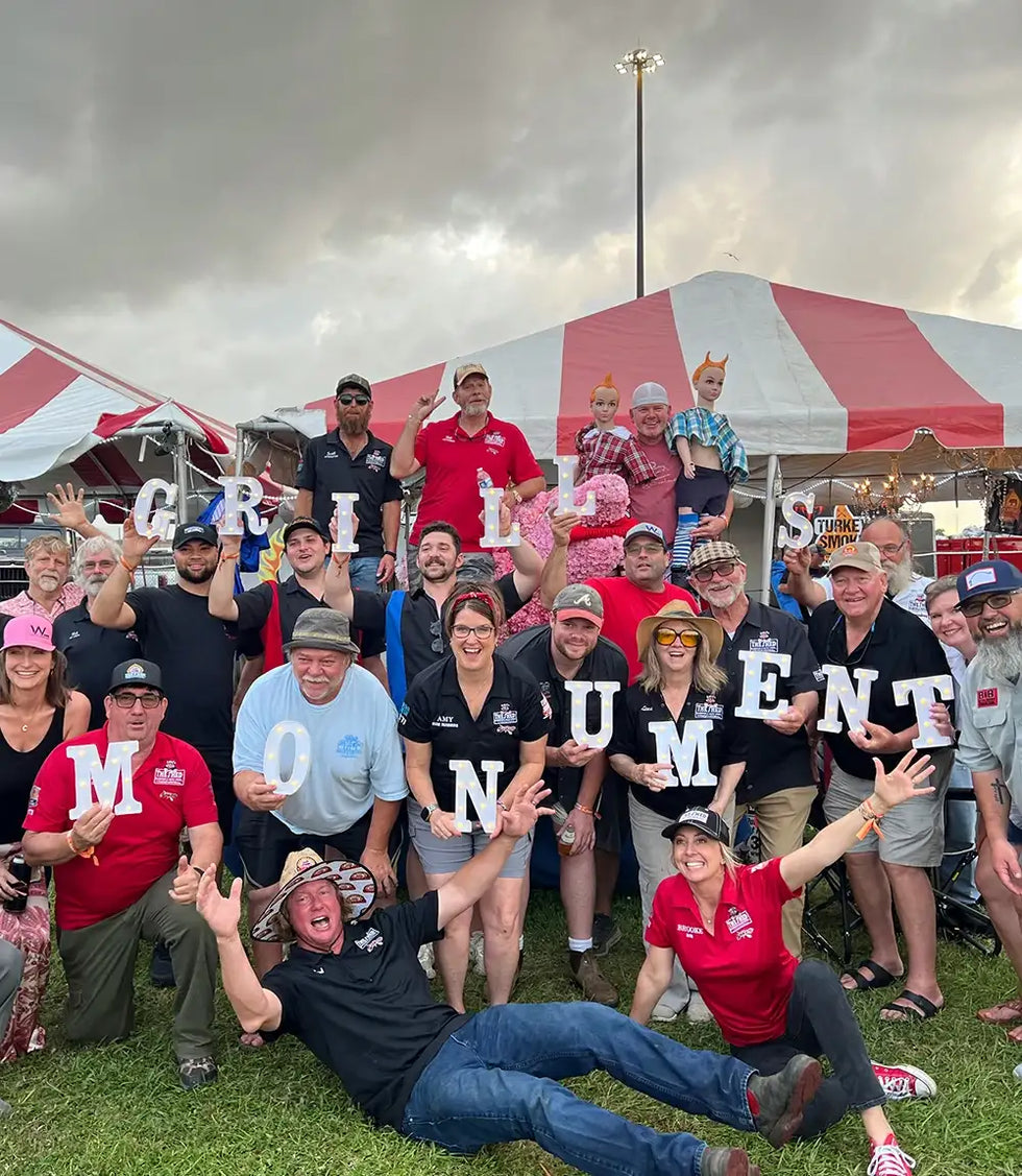 Group of people posing together with letters spelling 'MONUMENT GRILLS' at an outdoor event.
