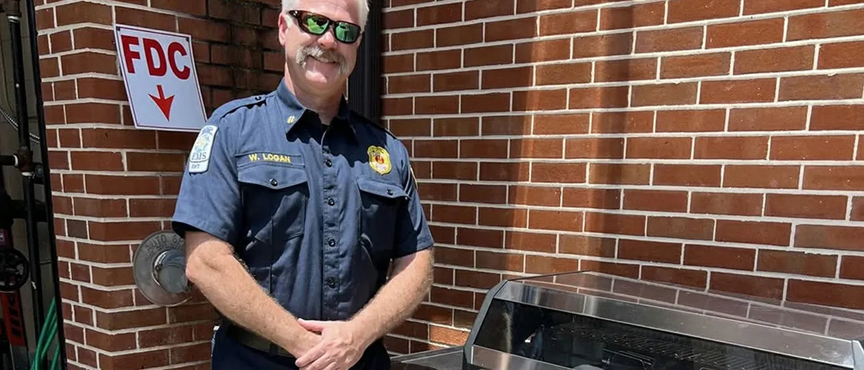 Man in a blue uniform standing next to a metal grill against a brick wall with an FDC sign.