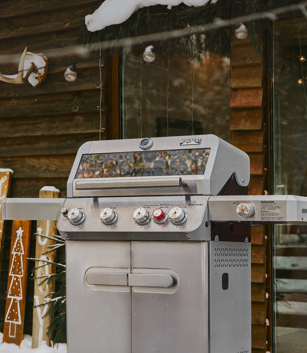 Outdoor grill in front of a wooden cabin with snow on the ground