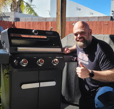 Man giving a thumbs up next to a black barbecue grill outdoors.