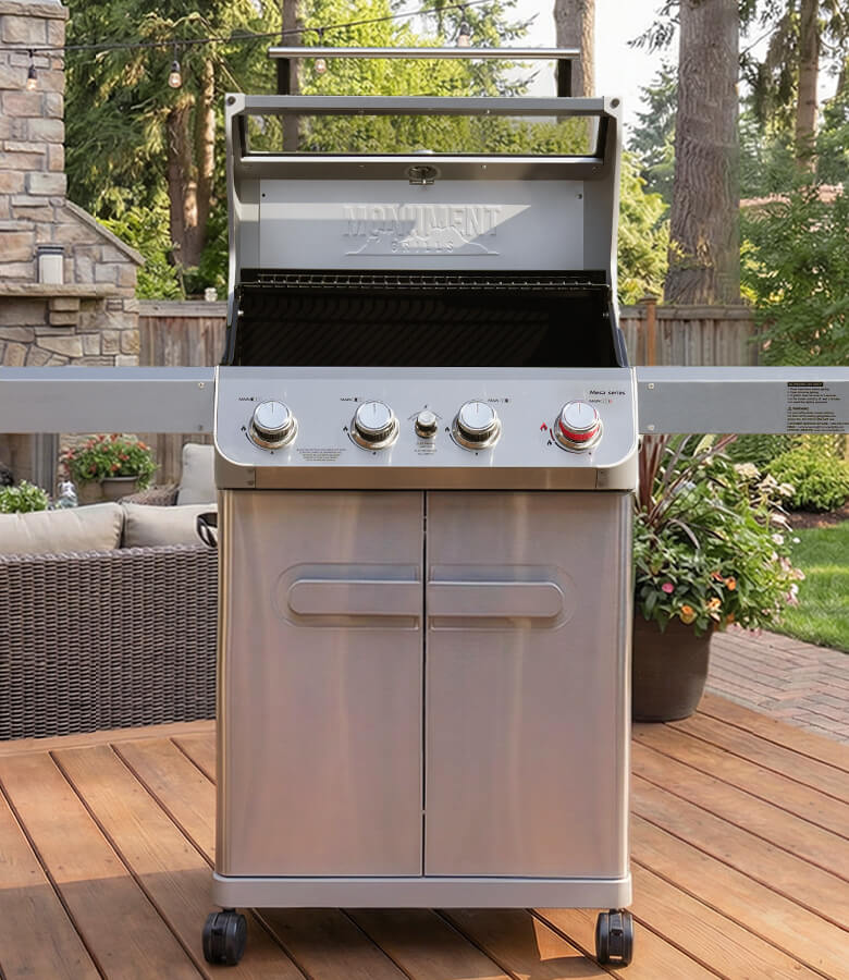 Stainless steel grill on a wooden deck with outdoor furniture and greenery in the background