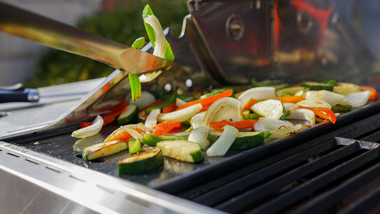 Vegetables being grilled on a barbecue with tongs