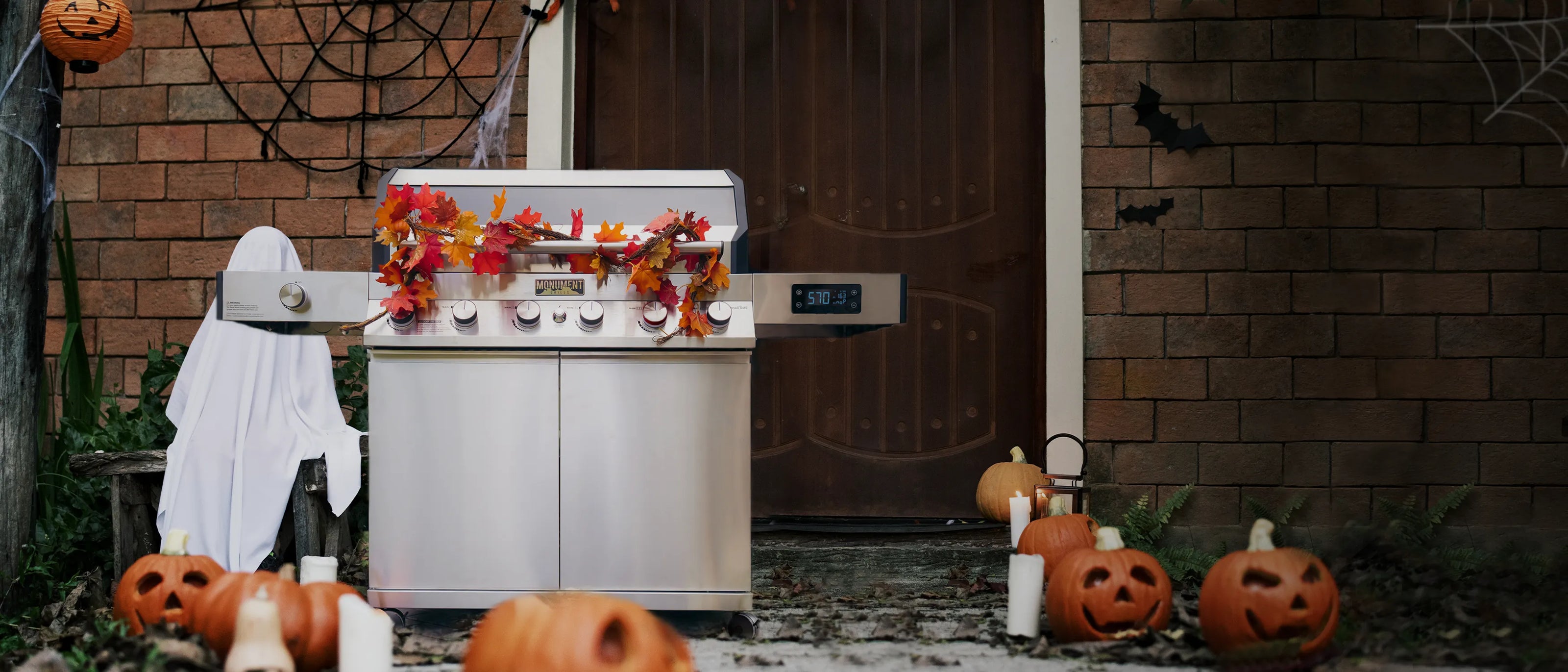 Outdoor grill decorated with Halloween decorations including pumpkins and a ghost, set against a brick wall.