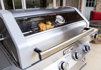 Stainless steel grill with chicken cooking inside, outdoor setting
