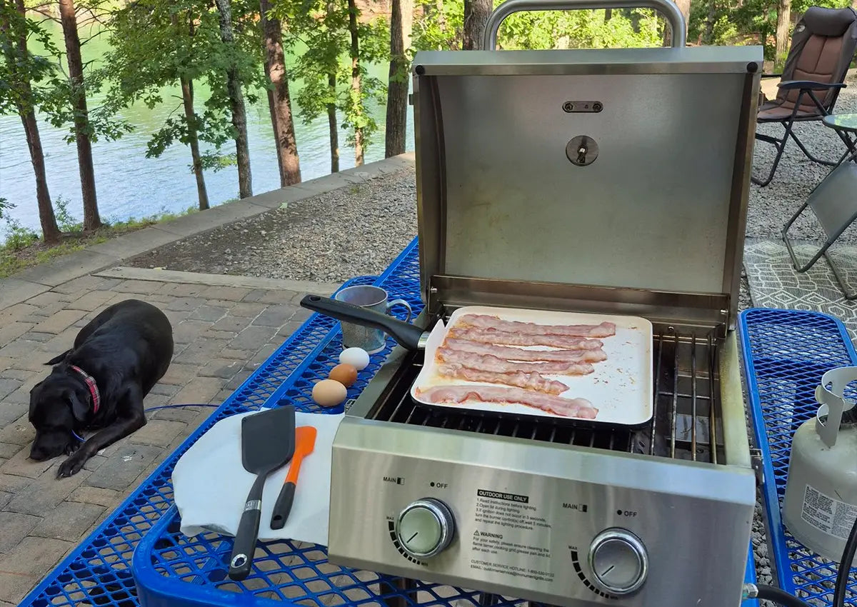 Grill with bacon cooking outdoors by a lake