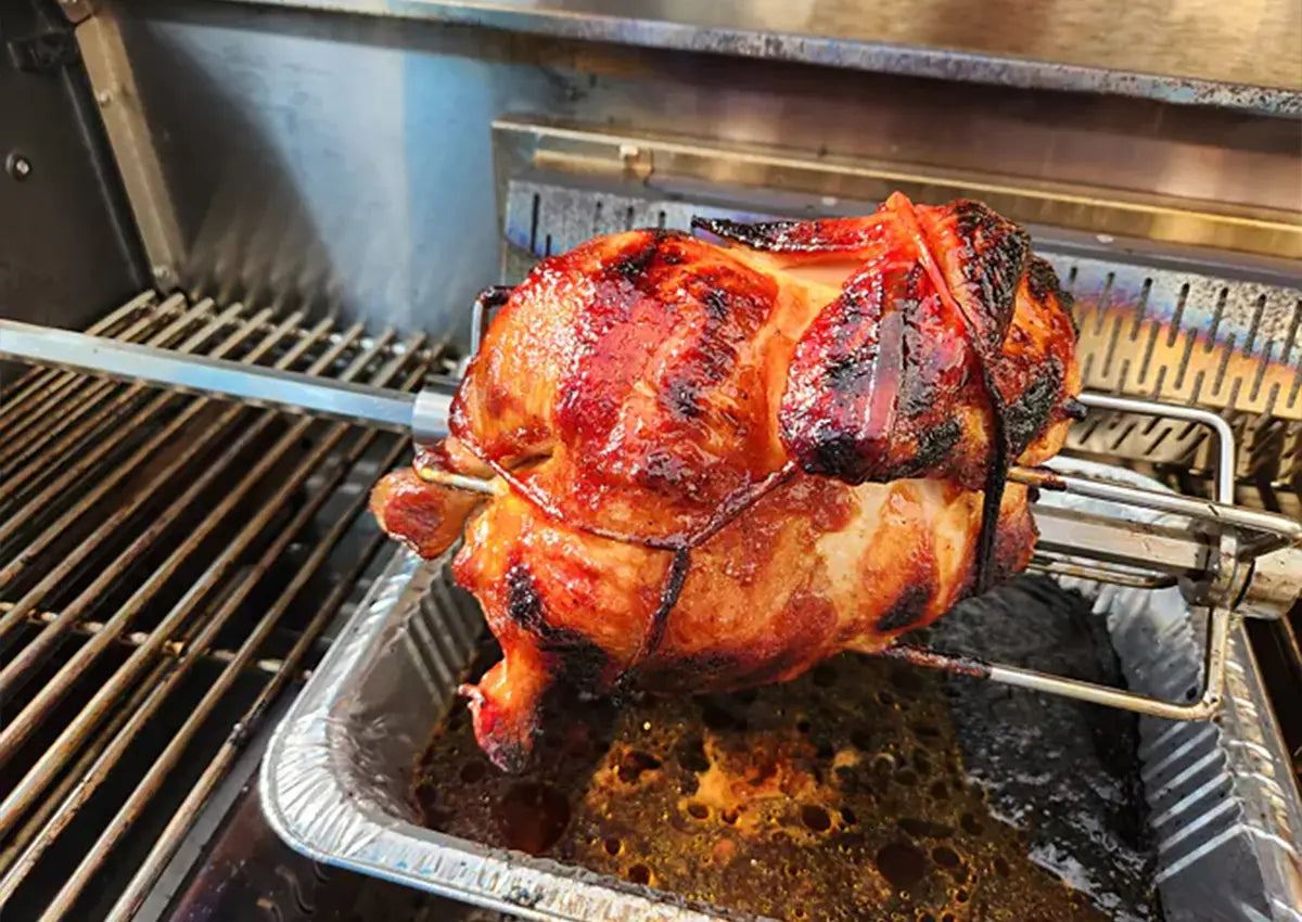 Roasted pork on a rotisserie over a metal tray on a grill