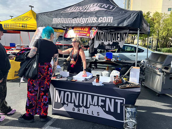 Person at a Monument Grills booth with a tent and table setup outdoors.