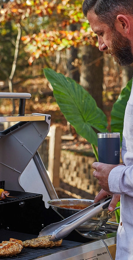 Man grilling outdoors with a blue tumbler in hand