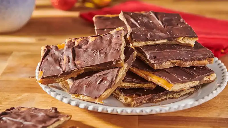 Chocolate-covered cracker toffee on a white plate with a wooden background