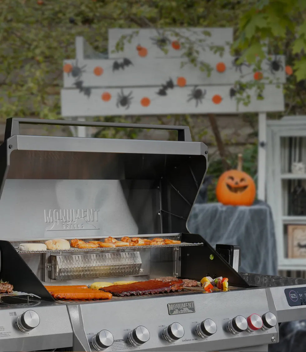 Outdoor grill with food being cooked, Halloween decorations in the background