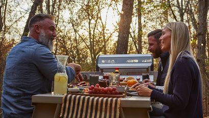 Family enjoying a meal outdoors with a grill in the background