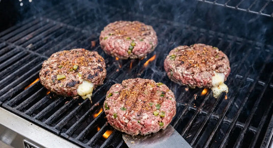 Four raw hamburger patties with cheese on a grill