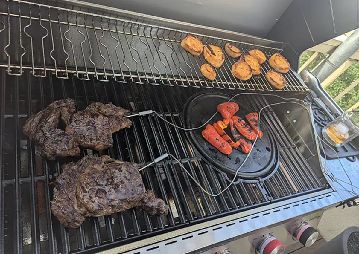 Grill with various food items including steaks, vegetables, and bread on a patio.