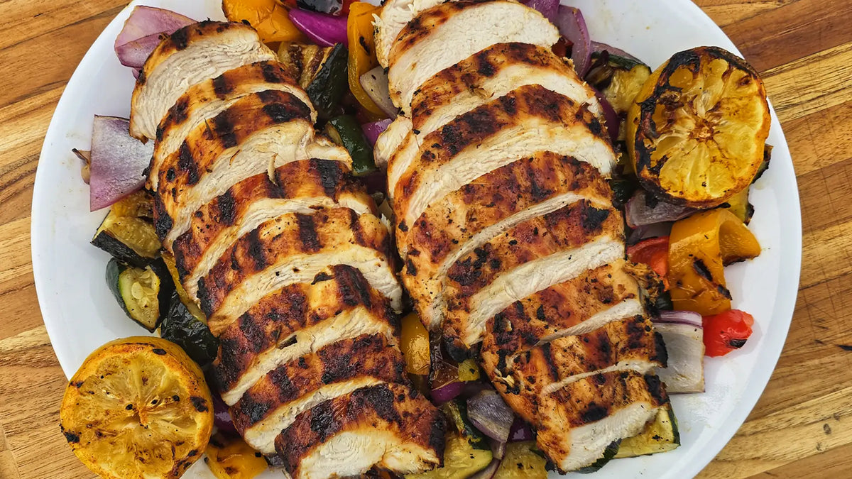Grilled chicken breast with vegetables on a white plate on a wooden table