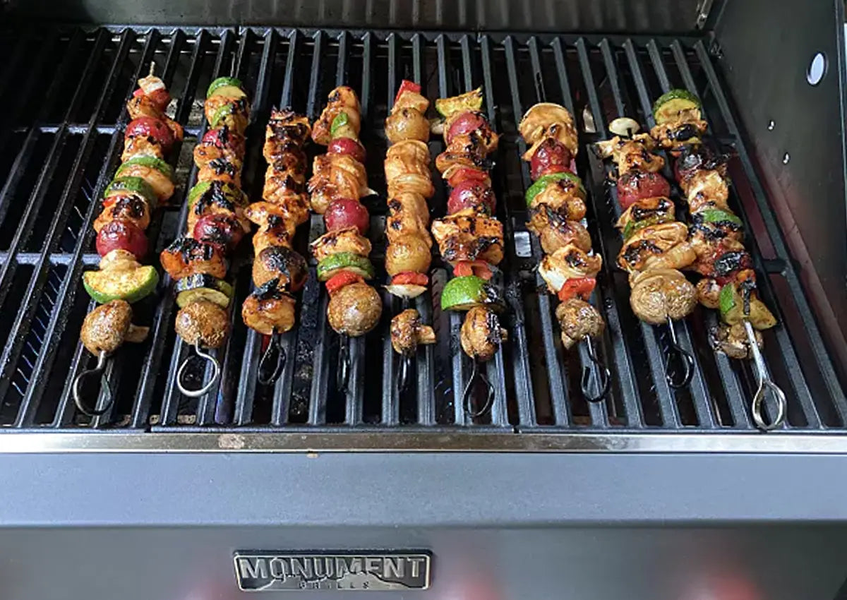 Grilled skewers on a barbecue with 'Monument' branding.