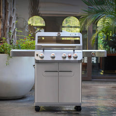 Stainless steel grill on a patio with plants and a glass door in the background