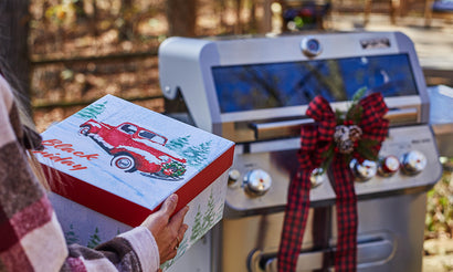Person holding a gift box with a red truck design in front of a grill decorated with Christmas ribbons.