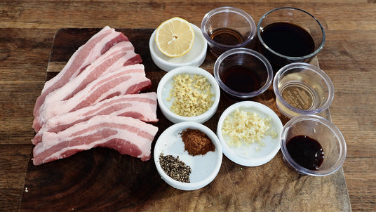 Raw bacon strips on a wooden cutting board with various seasonings in small containers.