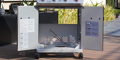 Outdoor grill with open lid showing interior components on a wooden deck.