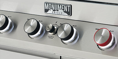 Control panel of a Monument grill with various knobs and a red and white knob.