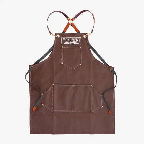 Brown apron with black straps on a white background, featuring 'Monument' branding.