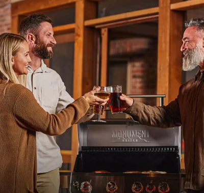 Three people toasting with drinks in front of a Monogram grill.