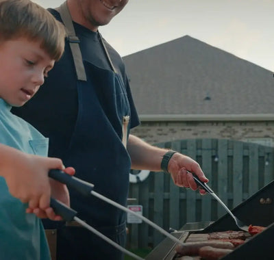Man and child grilling together outdoors with a house in the background