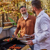 Two men grilling outdoors using the Mesa 415BZNG | Stainless Natural Gas Grill, surrounded by nature.