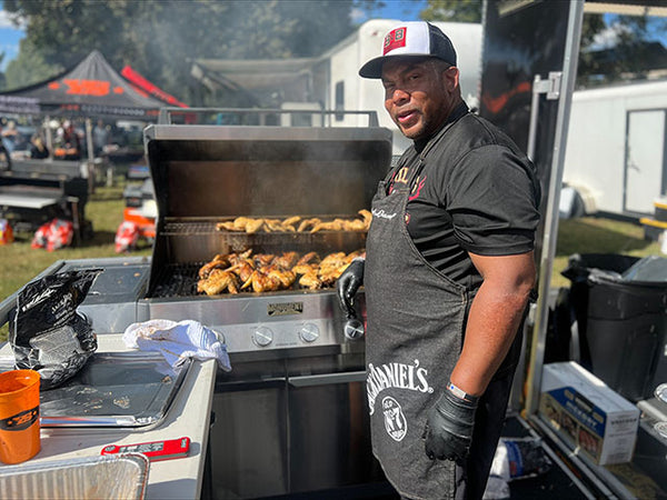 Man grilling food outdoors with a focus on the grill and his attire.