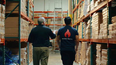 Two people walking through a warehouse with shelves stocked with boxes.